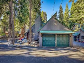 Nestled among tall pine trees, this charming property features a striking modern A-frame home with a distinctive green metal roof and a spacious two-car garage.