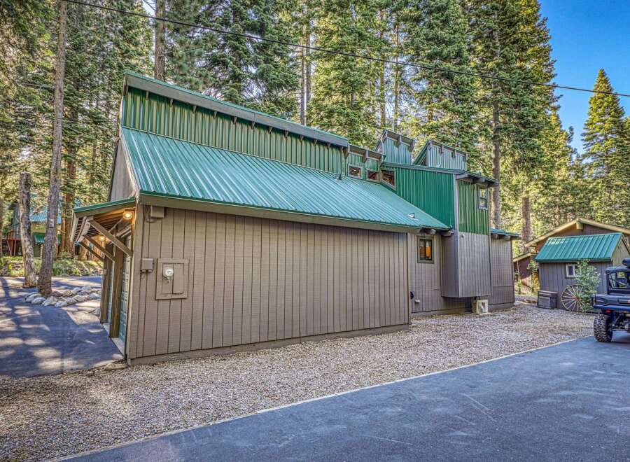 Discover this unique mountain home featuring a striking green metal roof and rustic siding, nestled amongst tall pine trees.