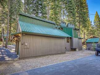 Discover this unique mountain home featuring a striking green metal roof and rustic siding, nestled amongst tall pine trees.