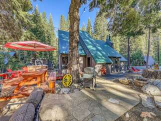 Escape to this charming cabin nestled in the woods, featuring a spacious wooden deck with a picnic table and umbrella, perfect for outdoor dining.