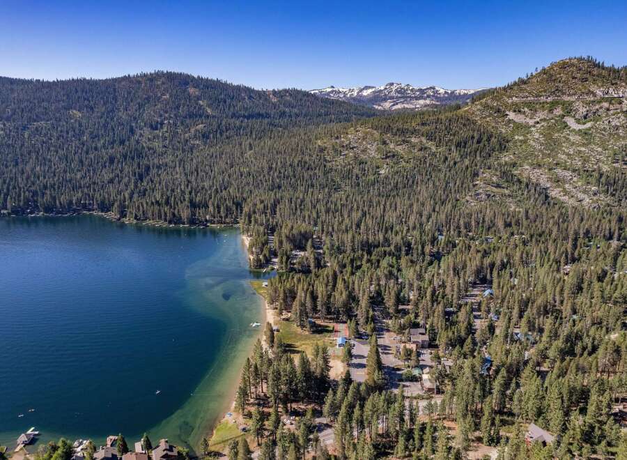 Experience the ultimate lakeside living with this stunning aerial view of a property nestled amidst a dense pine forest, offering direct access to a crystal-clear lake.