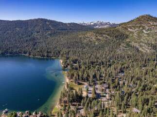 Experience the ultimate lakeside living with this stunning aerial view of a property nestled amidst a dense pine forest, offering direct access to a crystal-clear lake.