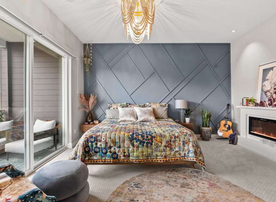 Experience bohemian luxury in this master bedroom, featuring a striking geometric accent wall and a vibrant, patterned quilt.