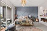 Experience bohemian luxury in this master bedroom, featuring a striking geometric accent wall and a vibrant, patterned quilt.