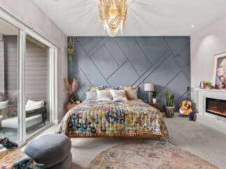 Experience bohemian luxury in this master bedroom, featuring a striking geometric accent wall and a vibrant, patterned quilt.