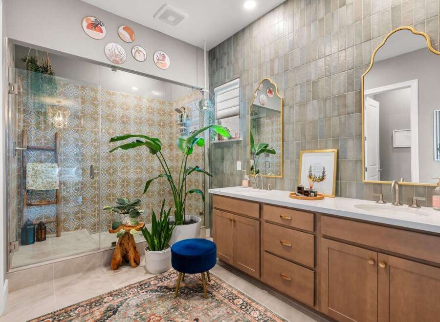 This stunning bathroom features a spacious glass-enclosed shower with intricate tilework, complemented by a large vanity with dual sinks and elegant gold-accented mirrors.