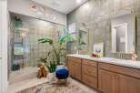 This stunning bathroom features a spacious glass-enclosed shower with intricate tilework, complemented by a large vanity with dual sinks and elegant gold-accented mirrors.
