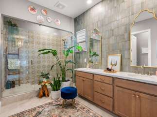 This stunning bathroom features a spacious glass-enclosed shower with intricate tilework, complemented by a large vanity with dual sinks and elegant gold-accented mirrors.