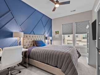 This bedroom features a striking blue accent wall with a geometric design, complemented by a plush tufted headboard and a comfortable gray comforter.