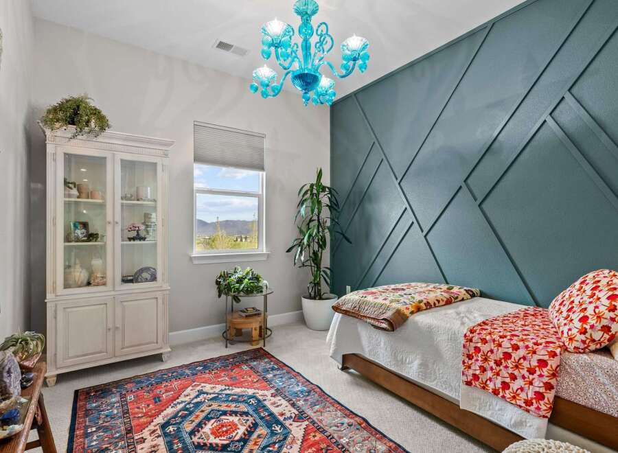 This charming bedroom features a striking teal accent wall with a geometric design, complemented by a vibrant, patterned rug and a unique blue glass chandelier.