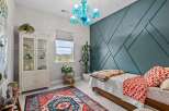 This charming bedroom features a striking teal accent wall with a geometric design, complemented by a vibrant, patterned rug and a unique blue glass chandelier.