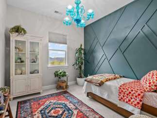 This charming bedroom features a striking teal accent wall with a geometric design, complemented by a vibrant, patterned rug and a unique blue glass chandelier.