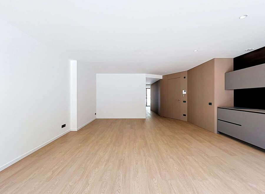 Discover this modern and spacious living area featuring a sleek, minimalist design with light wood flooring and clean white walls.