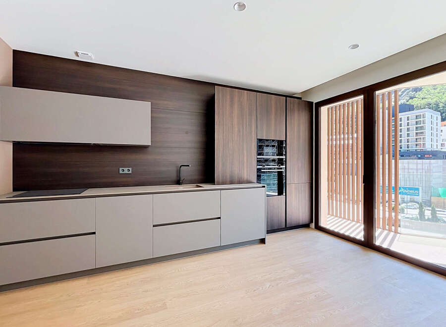 Discover this modern kitchen featuring sleek, handleless cabinetry in a sophisticated grey finish, complemented by a rich, dark wood-grained backsplash and integrated appliances.