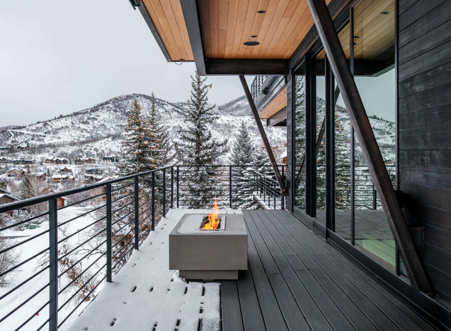 Experience luxury mountain living with this stunning contemporary home featuring a spacious deck overlooking a snow-covered landscape.