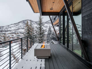 Experience luxury mountain living with this stunning contemporary home featuring a spacious deck overlooking a snow-covered landscape.