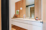 This modern bathroom vanity features a sleek white countertop with an integrated sink, complemented by warm wood paneling on the wall.