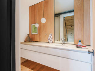 This modern bathroom vanity features a sleek white countertop with an integrated sink, complemented by warm wood paneling on the wall.