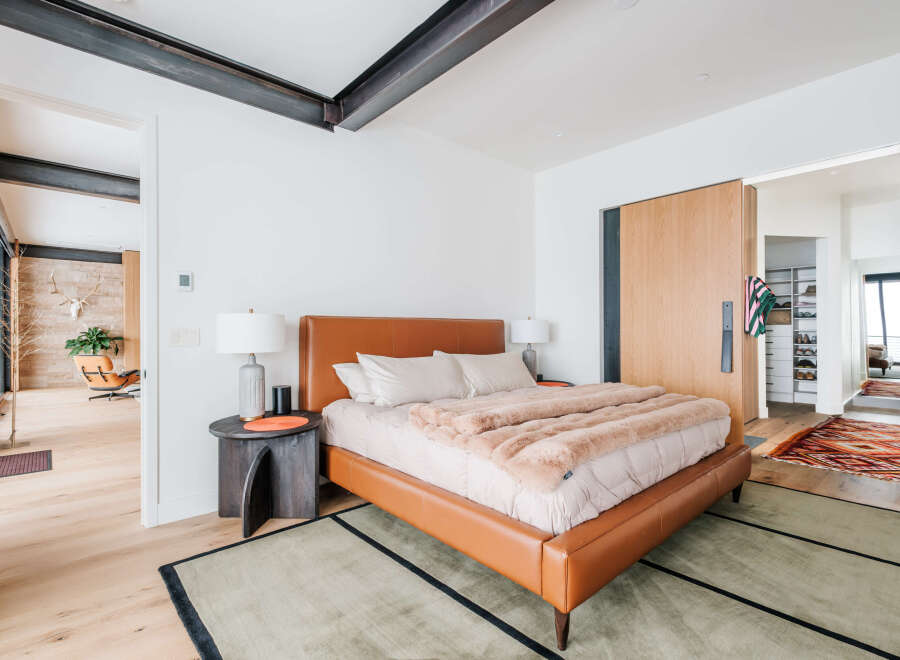 Experience modern luxury in this master bedroom featuring a sleek, cognac leather bed and plush, faux fur throw.