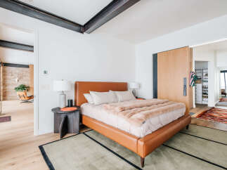 Experience modern luxury in this master bedroom featuring a sleek, cognac leather bed and plush, faux fur throw.