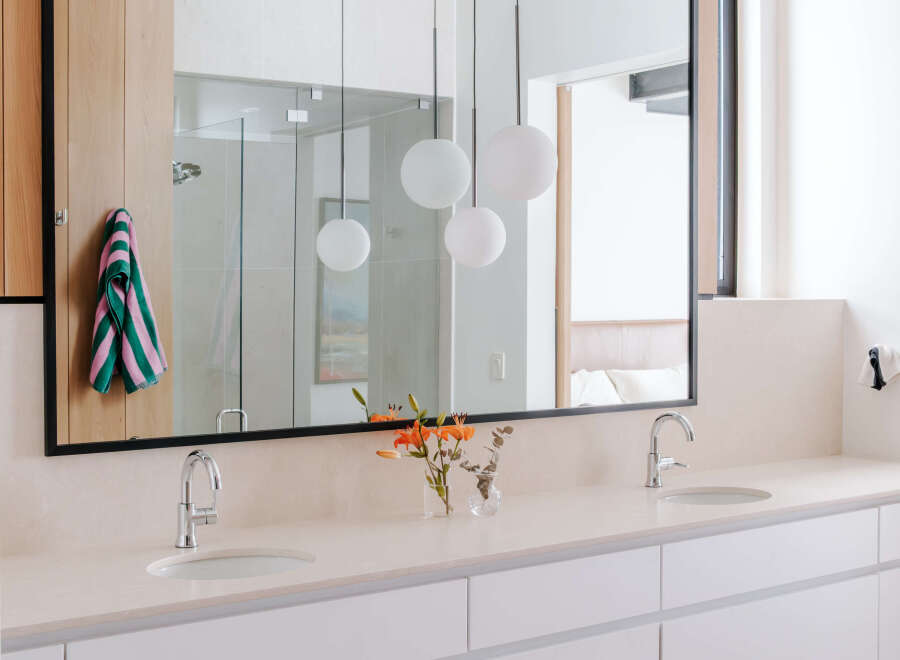 This modern bathroom features a spacious double vanity with sleek white cabinetry and a light-colored stone countertop.