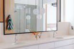 This modern bathroom features a spacious double vanity with sleek white cabinetry and a light-colored stone countertop.