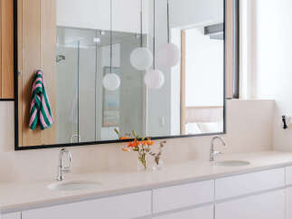 This modern bathroom features a spacious double vanity with sleek white cabinetry and a light-colored stone countertop.