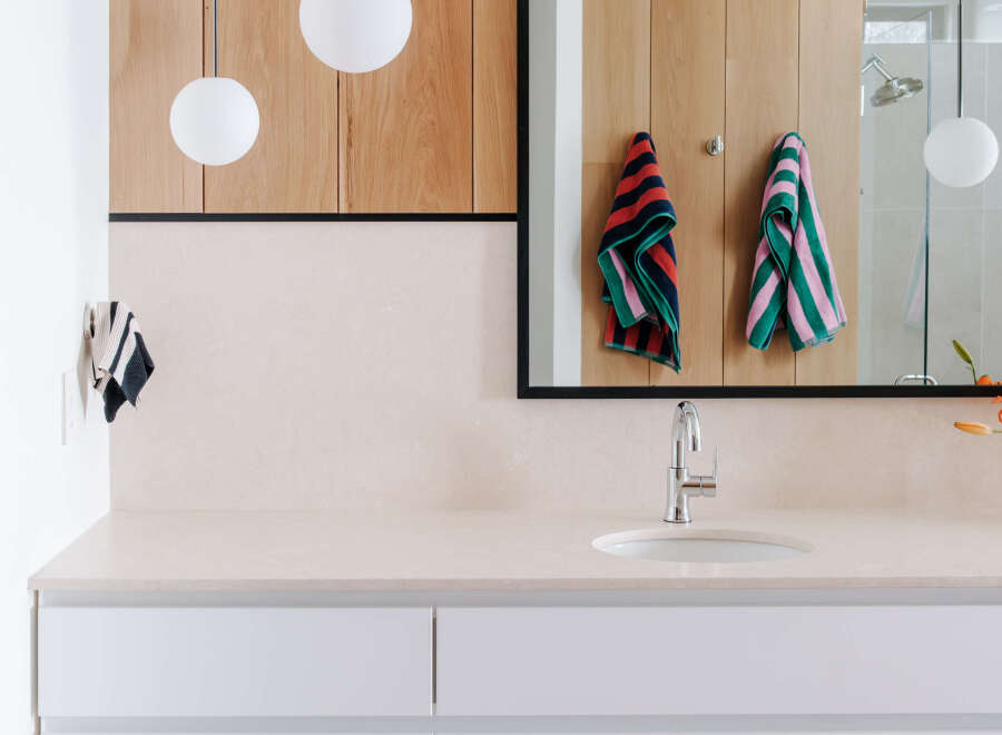 This modern bathroom features a sleek vanity with white drawers and a light-colored countertop, complemented by warm wood cabinetry above.