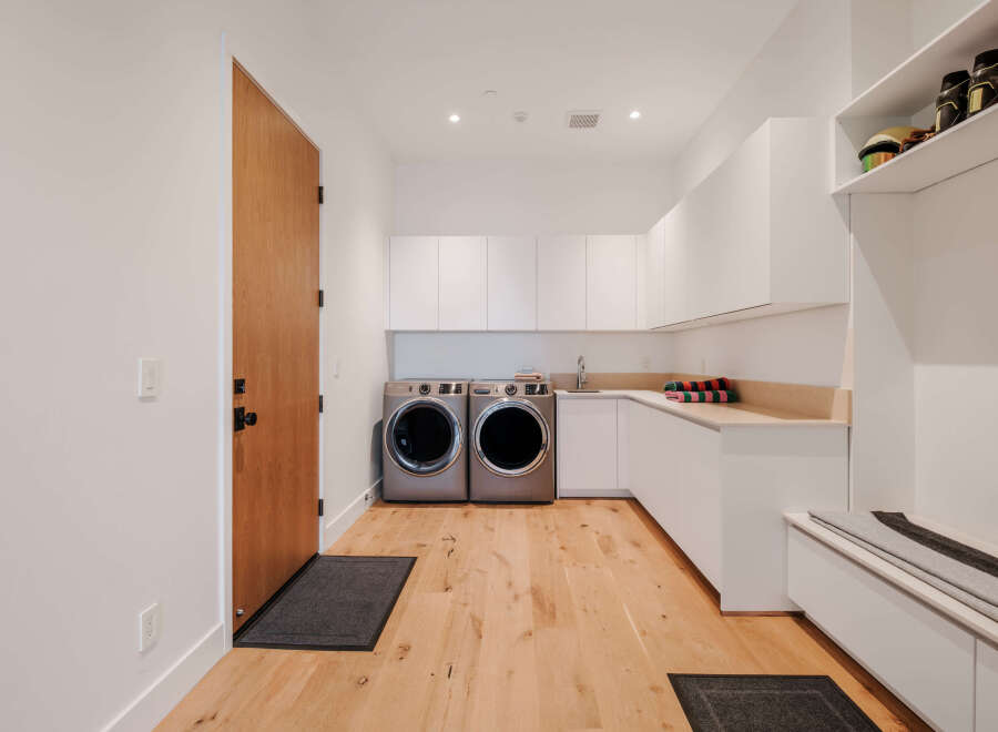 This modern laundry room features sleek white cabinetry and a built-in bench with storage, perfect for a mudroom area.