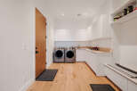This modern laundry room features sleek white cabinetry and a built-in bench with storage, perfect for a mudroom area.