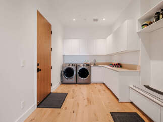 This modern laundry room features sleek white cabinetry and a built-in bench with storage, perfect for a mudroom area.