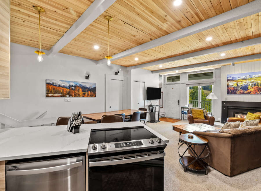 Experience modern mountain living in this beautifully appointed condo, featuring a stunning wood-paneled ceiling and a sleek kitchen island with a built-in stovetop.
