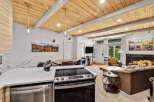 Experience modern mountain living in this beautifully appointed condo, featuring a stunning wood-paneled ceiling and a sleek kitchen island with a built-in stovetop.