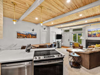 Experience modern mountain living in this beautifully appointed condo, featuring a stunning wood-paneled ceiling and a sleek kitchen island with a built-in stovetop.