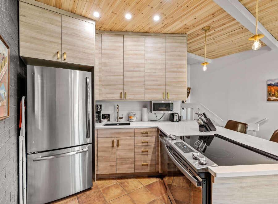 This modern kitchen boasts sleek, light wood cabinetry with brushed gold hardware, complemented by a stainless steel refrigerator and a stylish induction stovetop.