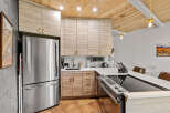 This modern kitchen boasts sleek, light wood cabinetry with brushed gold hardware, complemented by a stainless steel refrigerator and a stylish induction stovetop.