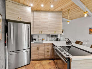 This modern kitchen boasts sleek, light wood cabinetry with brushed gold hardware, complemented by a stainless steel refrigerator and a stylish induction stovetop.