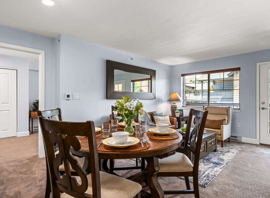 Experience comfortable dining and living in this inviting space, featuring a round wooden dining table set for four and a cozy living area with plush seating.