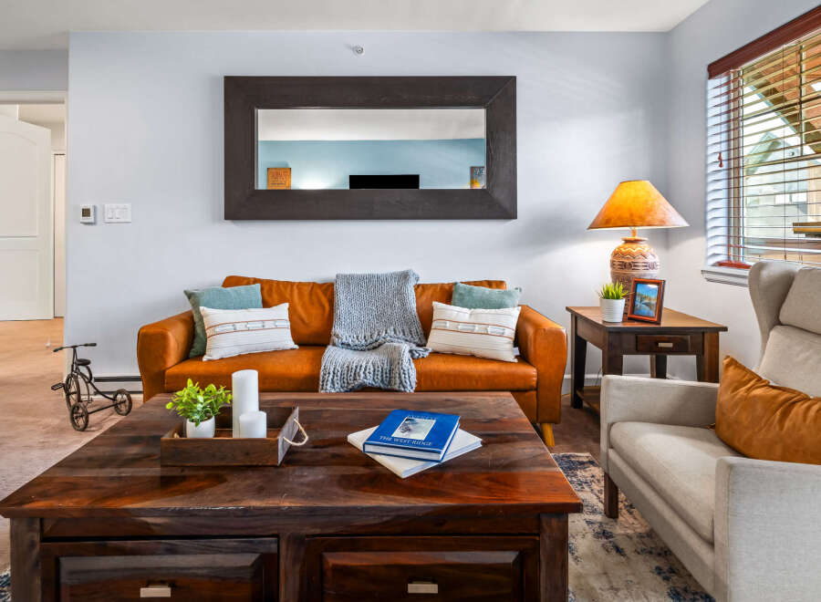 Step into this inviting living room, featuring a warm, caramel-colored leather sofa complemented by plush throw pillows and a cozy knit blanket.