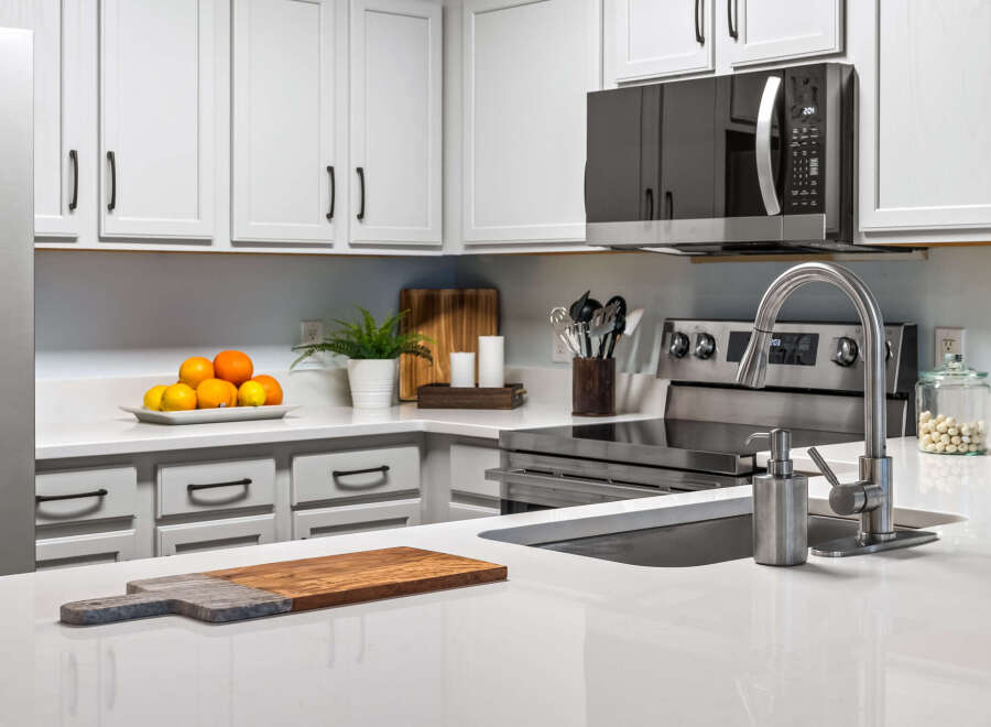 This modern kitchen boasts sleek white cabinetry and a spacious quartz countertop, perfect for meal preparation.