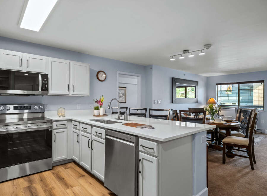 This modern kitchen features sleek white cabinetry, a spacious island with a built-in sink and dishwasher, and stainless steel appliances including a microwave and oven.