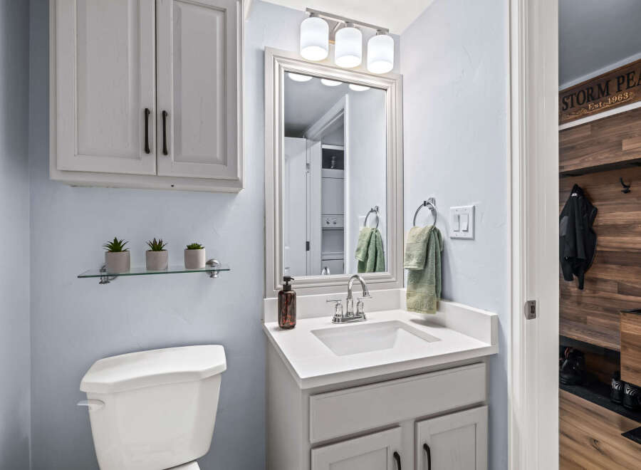 This charming bathroom features a clean white vanity with a modern sink and faucet, complemented by a large framed mirror and a trio of vanity lights.