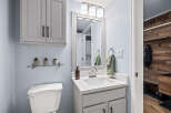 This charming bathroom features a clean white vanity with a modern sink and faucet, complemented by a large framed mirror and a trio of vanity lights.