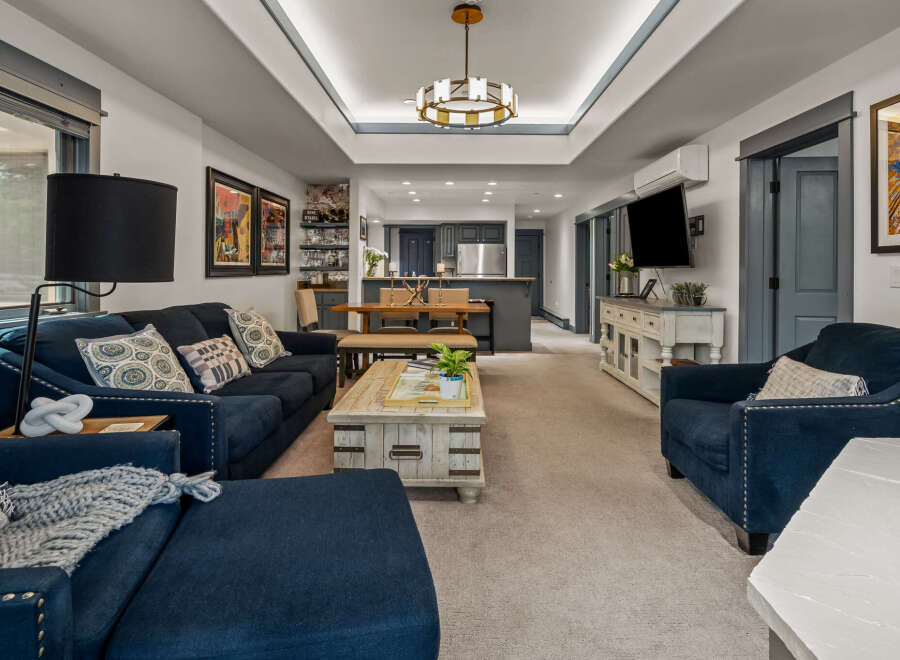 Experience modern living in this spacious open-concept home, featuring a stylish living area with plush navy seating and a unique distressed wood coffee table.