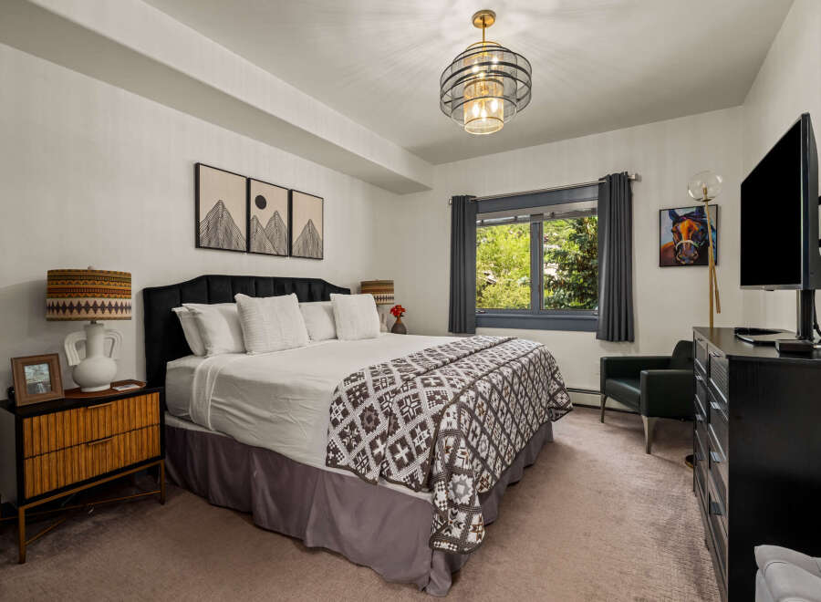 Experience ultimate comfort in this beautifully appointed bedroom, featuring a plush king-size bed adorned with crisp white linens and a striking geometric-patterned throw.