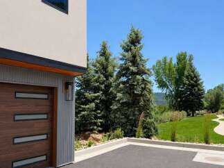This modern home features a striking garage door with horizontal wood panels and sleek glass inserts, complemented by a contemporary exterior light fixture.