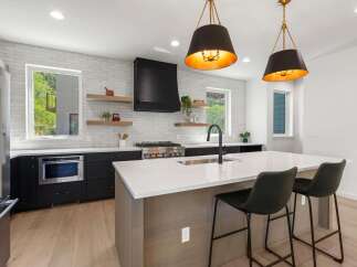 Experience modern luxury in this stunning kitchen, featuring sleek black cabinetry, a spacious island with a waterfall countertop, and a professional-grade gas range.