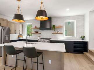 Experience modern luxury in this stunning kitchen, featuring sleek dark cabinetry, a spacious island with a waterfall countertop, and elegant pendant lighting.