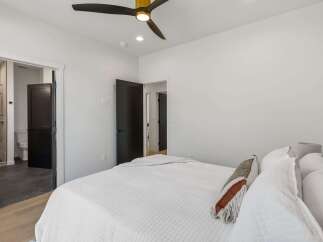 Experience modern comfort in this inviting bedroom, featuring a plush white quilted bed and a stylish ceiling fan with a gold accent.