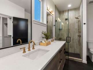 Experience modern luxury in this stunning bathroom featuring a dual vanity with elegant gold fixtures and a spacious walk-in shower with vertical tilework.